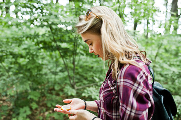Portrait of an attractive blond girl posing with a compass in a forest.