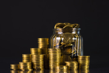 Coins stacks and gold coin money in the glass jar on dark background, for saving for the future banking finance concept.