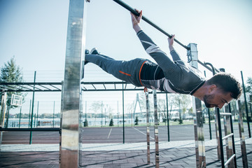 Professional sportsman doing the chin ups with his eyes clothes