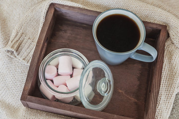 Cup of coffee on rustic wooden tray, sweet marshmallow and warm woolen sweater. Cozy autumn or winter weekend or holidays at home. Fall home decoration with hot drink mug. Hygge morning style concept