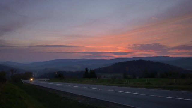 Car on the road between hills. Beautiful sunset with colorful sky.
