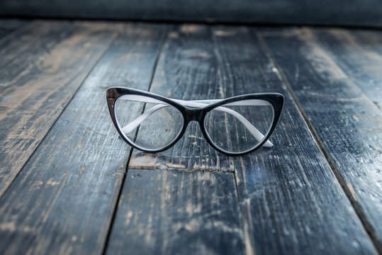 women's glasses lie on a dark wooden surface