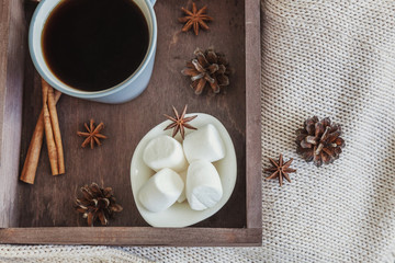 Cup of coffee on rustic wooden tray, sweet marshmallow and warm woolen sweater. Cozy autumn or winter weekend or holidays at home. Fall home decoration with hot drink mug. Hygge morning style concept