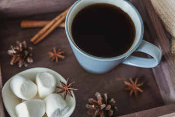 Cup of coffee on rustic wooden tray, sweet marshmallow and warm woolen sweater. Cozy autumn or winter weekend or holidays at home. Fall home decoration with hot drink mug. Hygge morning style concept