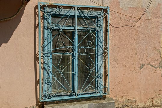 old window with blue grille on brown wall