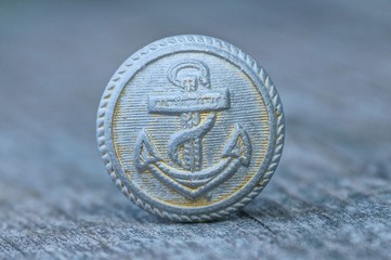 big old gray round button with an anchor on the table