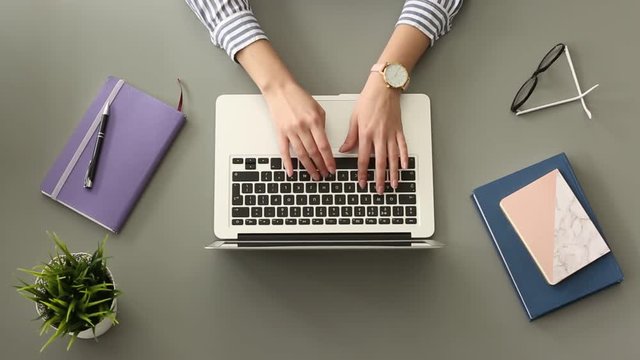 Woman typing on laptop keyboard at table, top view
