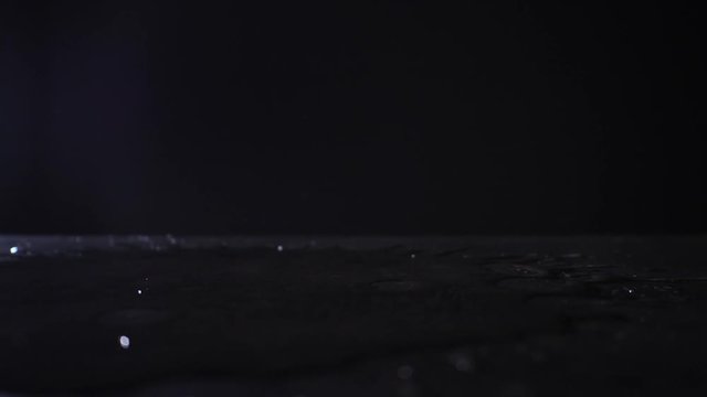 Water pouring onto dark table, closeup

