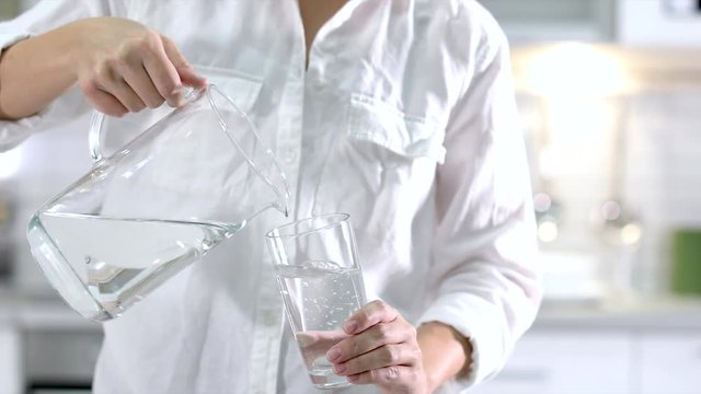 Woman pouring water from jug into glass indoors, closeup
