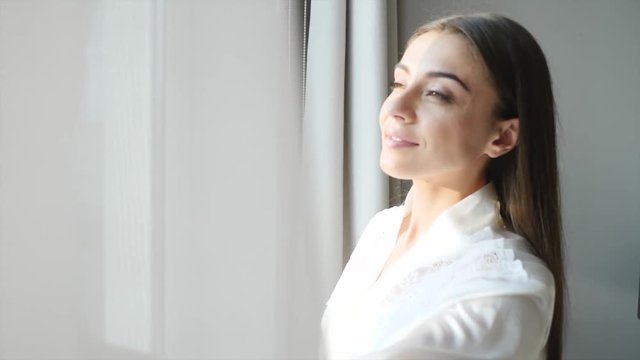Young woman opening curtains at home on sunny morning
