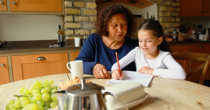 Grandmother helping granddaughter in studies in kitchen 4k