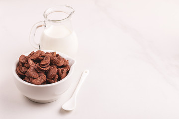 Crunchy chocolate corn flakes in bowl with jar of milk