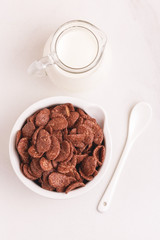 Crunchy chocolate corn flakes in bowl with jar of milk
