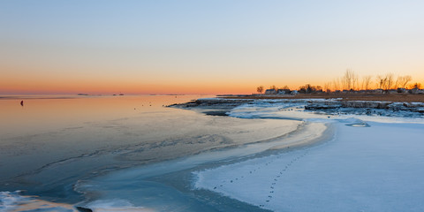 Sunrise on frozen sea on New England coast with footprints on snow from wandering animals