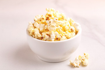 Tasty salty popcorn in bowl on light marble backgraund