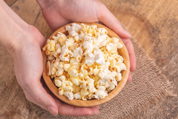 Tasty salty popcorn in wooden bowl in woman's hands.