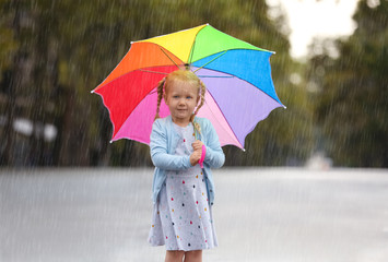 Portrait of cute little girl with umbrella in city on rainy day