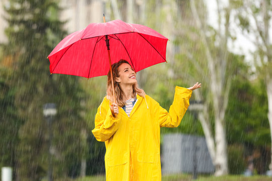 Portrait of happy young woman with red umbrella in park on rainy day
