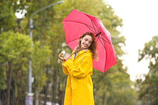 Portrait of young woman with red umbrella in city on rainy day