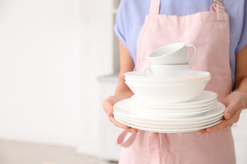 Woman with clean dishes and cups in kitchen, closeup. Space for text