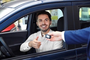 Young salesman giving car key to client in dealership