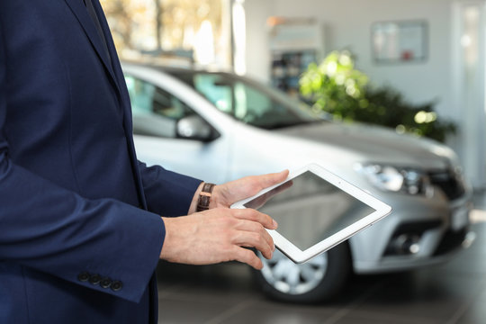 Young car salesman with tablet in dealership, closeup