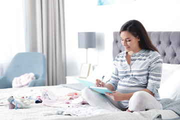 Pregnant woman writing packing list for maternity hospital on bed at home