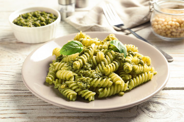 Plate with delicious basil pesto pasta on wooden table