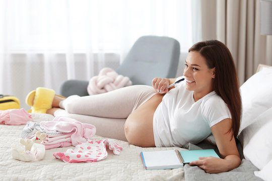 Pregnant woman writing packing list for maternity hospital on bed at home