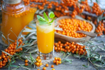 Homemade buckthorn soft drink in a glass and ripe sea buckthorn berries on the table. Healthy and diet food. Seabuckthorn, a spoon with berries and a glass of juice.