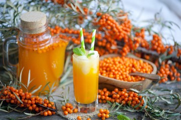 Homemade buckthorn soft drink in a glass and ripe sea buckthorn berries on the table. Healthy and diet food. Seabuckthorn, a spoon with berries and a glass of juice.