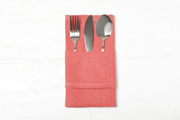 Folded napkin with fork, spoon and knife on white wooden background, top view