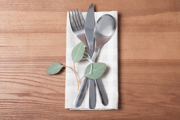 Napkin with fork, spoon and knife on wooden background, top view