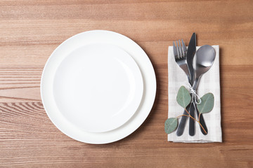 Table setting with plates, cutlery and napkin on wooden background, top view