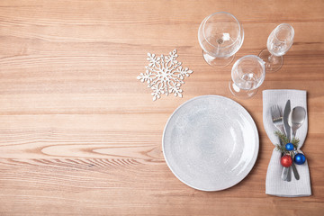 Christmas table setting with plate, glasses, cutlery and napkin on wooden background, flat lay....