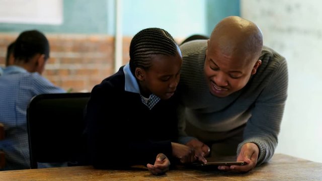 Male teacher using digital tablet with student in classroom 4k