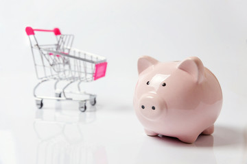 Small supermarket grocery push cart for shopping with piggy bank isolated on white background. Sale...