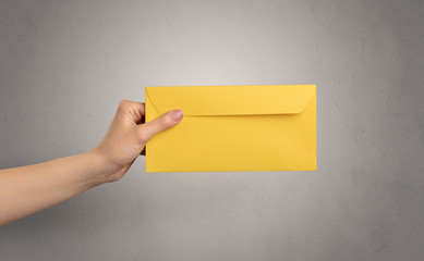 Female hand holding coloured and white envelope with empty wall background 