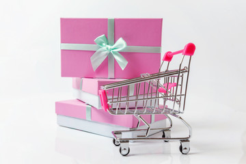 Small supermarket grocery push cart for shopping toy with pink gift box isolated on white background. Sale buy mall market shop consumer concept. Copy space