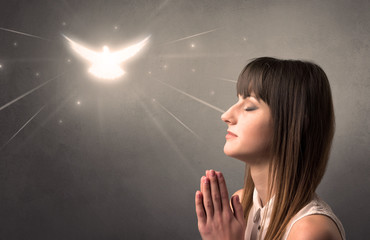 Young woman praying on a grey background with a sparkling bird above her
