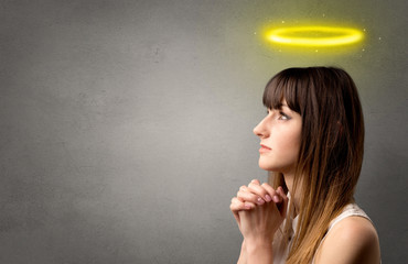 Young woman praying on a grey background with a shiny yellow halo above her head