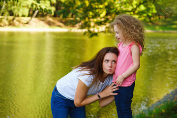 Family time. Mother and daughter play by the river. Woman put ear to little girl's belly