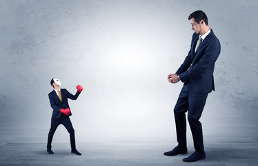 Big businessman being afraid of small masked businessman with box gloves in an empty room concept
