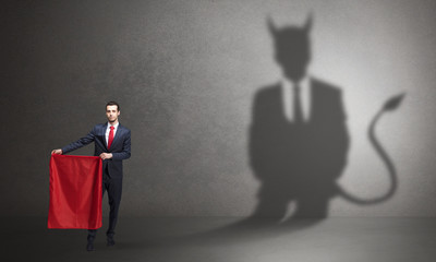 Businessman standing with red cloth in his hand and devil shadow on the background
