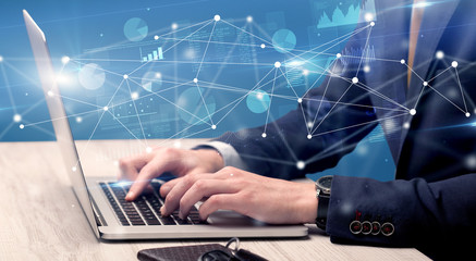 Businessman typing on laptop with linked reports charts grapghs around
