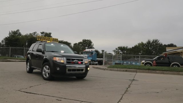 Safety vehicle with red mesh flags driving ahead of loaded oversized Peterbilt truck.