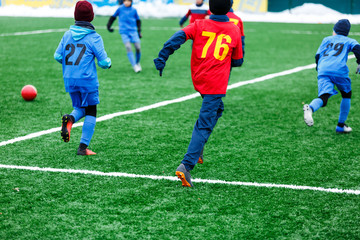 Young Active sport heathy boys in red and blue sportswear running and kicking a red ball on football field with artificial turf. soccer youth team plays football. activities for kids, training