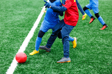 Fototapeta premium Boys in red and blue sportswear kicking soccer ball on green grass field. youth football game. Children sport competition, kids plays outdoor, winter activities, training
