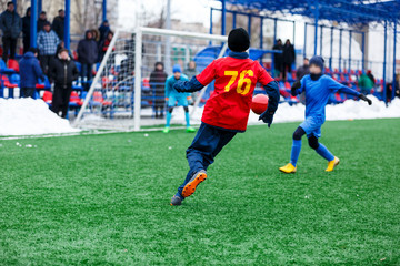 Young Active sport heathy boys in red and blue sportswear running and kicking a red ball on football field with artificial turf. soccer youth team plays football. activities for kids, training