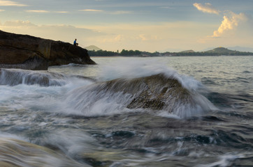 summer activity, a man catch the fish like a fisherman in strong and high wave hit the stone in foreground